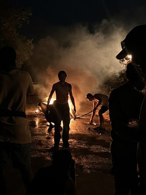 Silhouetted figures near smoky fire at night